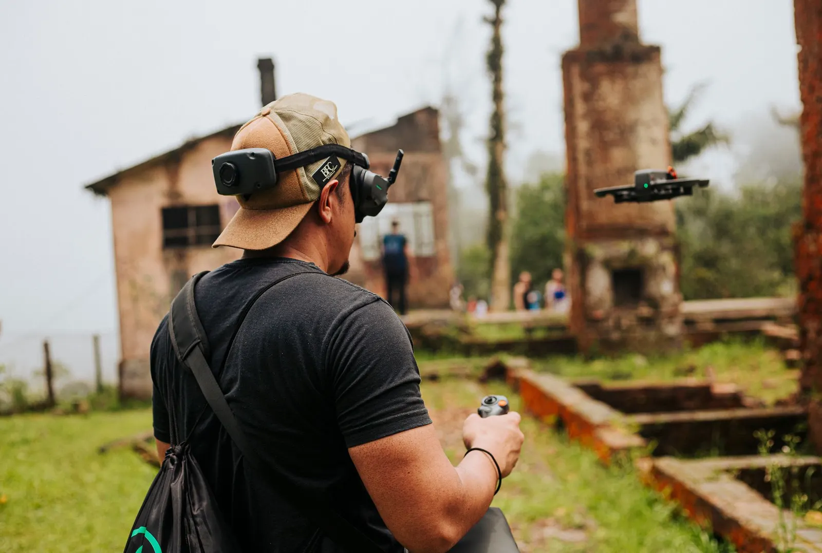A man uses a drone in a misty, abandoned building site surrounded by greenery.
